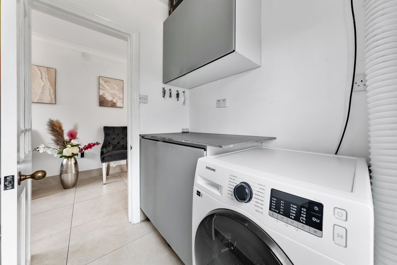 Modern laundry room with white washing machine, gray cabinetry, and open doorway to living area