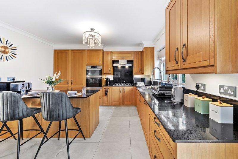 Modern kitchen with wooden cabinetry, black countertops, stainless steel appliances and dining chairs