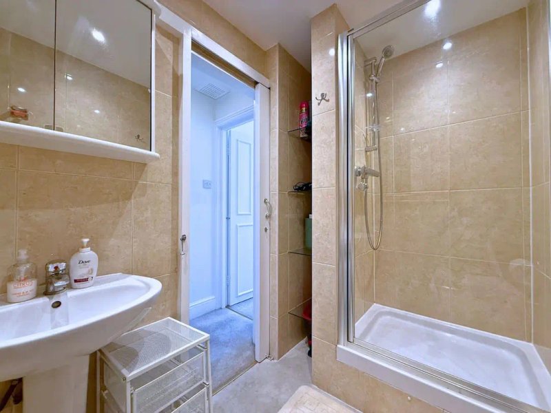 Bathroom with beige tile walls, white sink, mirror cabinet, shower enclosure and toilet