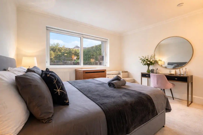 Bright bedroom with double bed, round mirror, desk, and large window overlooking trees