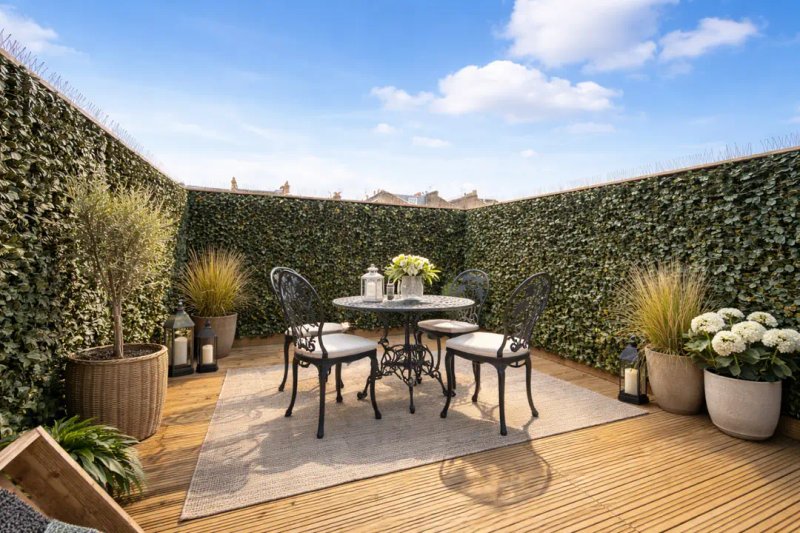 Outdoor terrace with round dining table, chairs, potted plants and ivy-covered walls