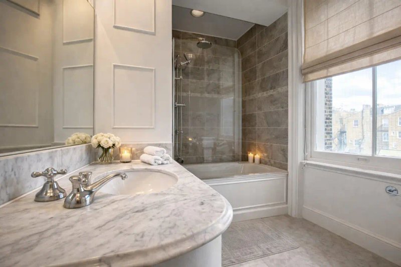 Bright bathroom with marble countertop, glass shower enclosure, window overlooking city skyline