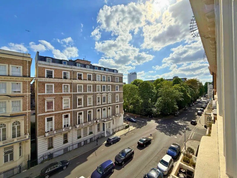 Urban street view with period apartment buildings, parked cars, and blue sky