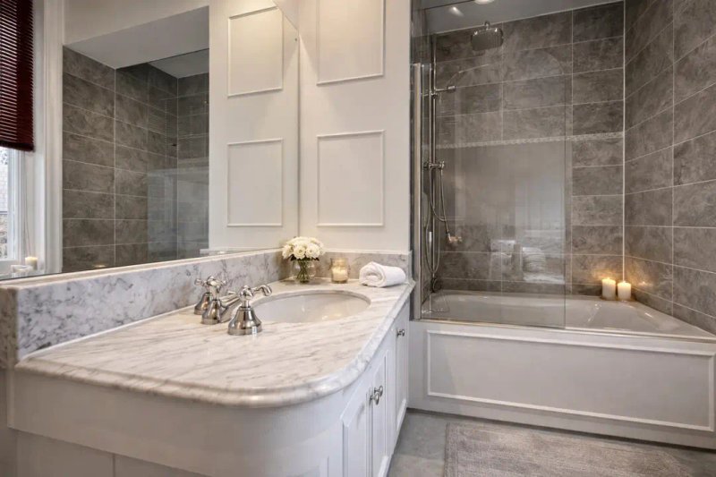 Modern bathroom with marble countertop, white vanity, glass shower enclosure and tile walls