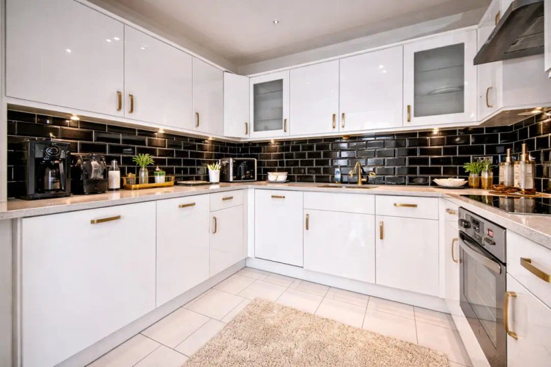 Modern white kitchen with black tile backsplash, built-in oven, and countertop appliances