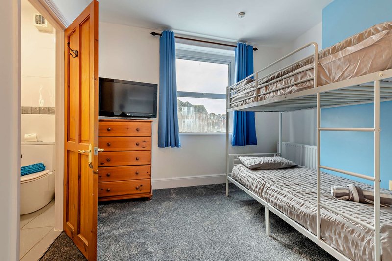 Bedroom with bunk beds, wooden dresser, TV, blue curtains and grey carpet