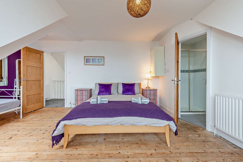Bright attic bedroom with double bed, purple bedding, wooden floors and ensuite bathroom