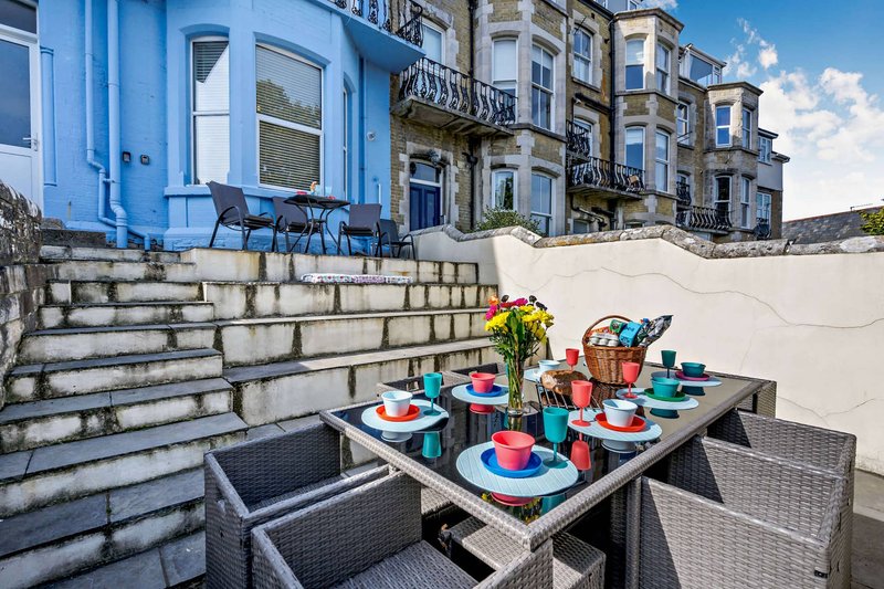 Outdoor terrace with dining table, colorful place settings, flowers, and Victorian townhouses in background