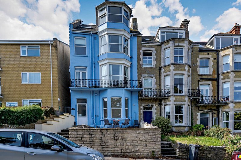 Street-facing exterior of Victorian terraced houses with blue facade, bay windows and parked car