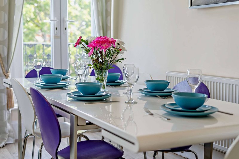 Dining table set with purple chairs, teal tableware, floral centerpiece and windows