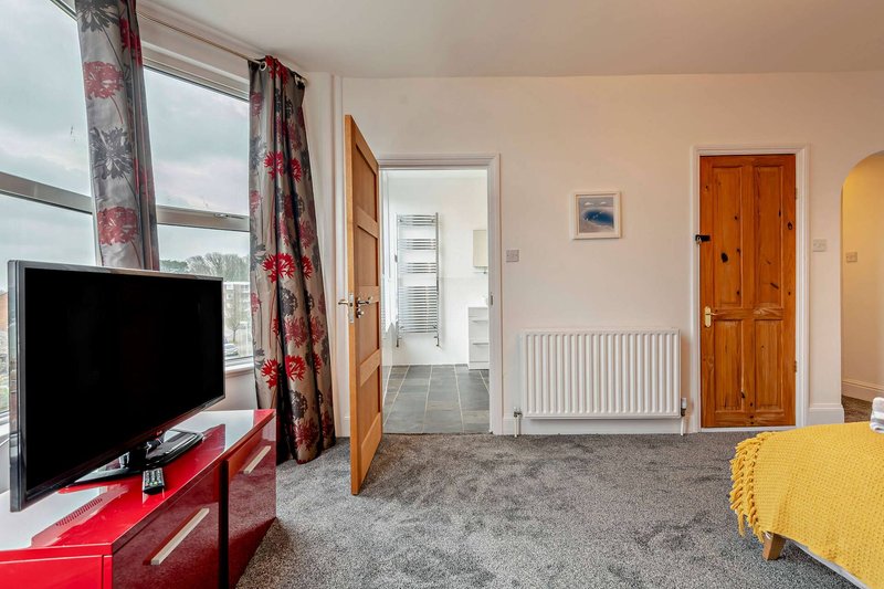 Bright bedroom with TV, red unit, floral curtains, wooden doors and yellow bedding