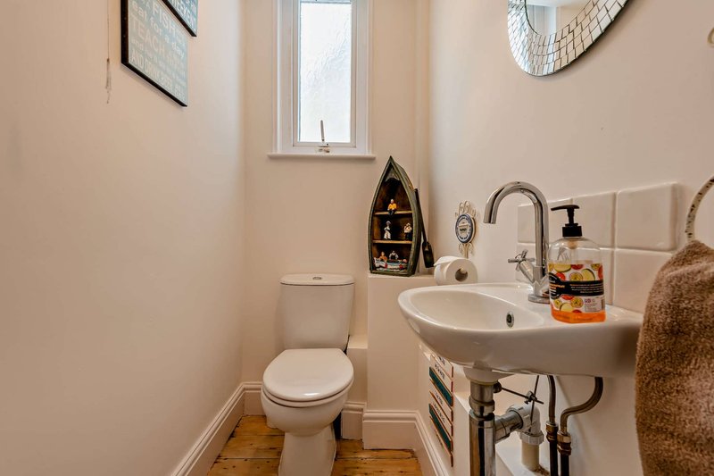 Small bathroom with toilet, pedestal sink, window, and wooden flooring