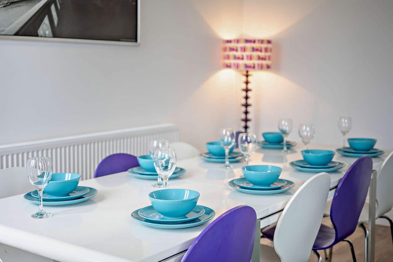 Dining room with white table, purple and white chairs, blue tableware and glasses
