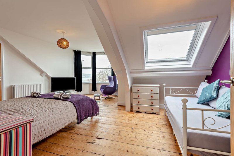 Bright attic bedroom with purple accent wall, wooden floor, double bed and skylight window