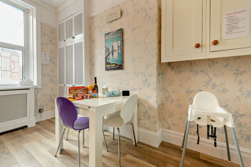 Compact kitchen-dining area with white table, purple and cream chairs, high chair, and floral wallpaper