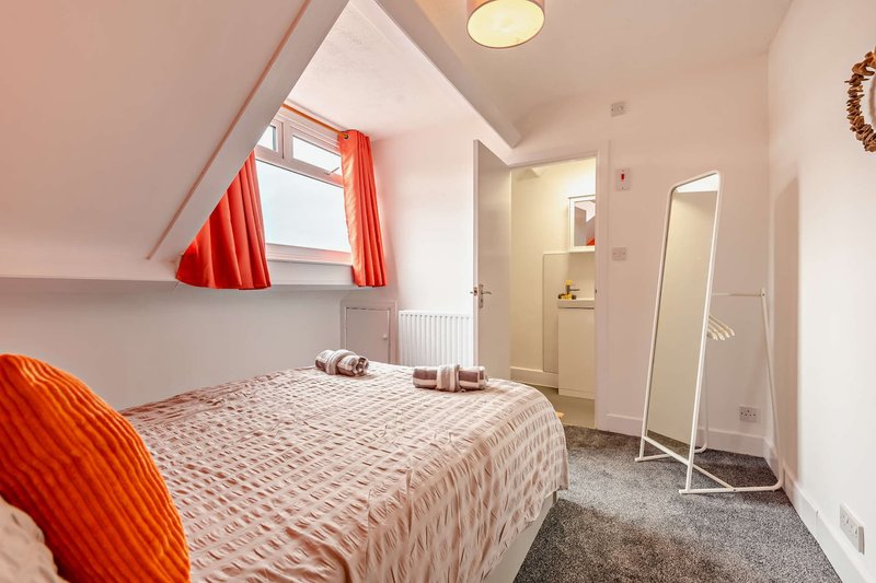 Bright attic bedroom with double bed, red curtains, mirror and en-suite bathroom door