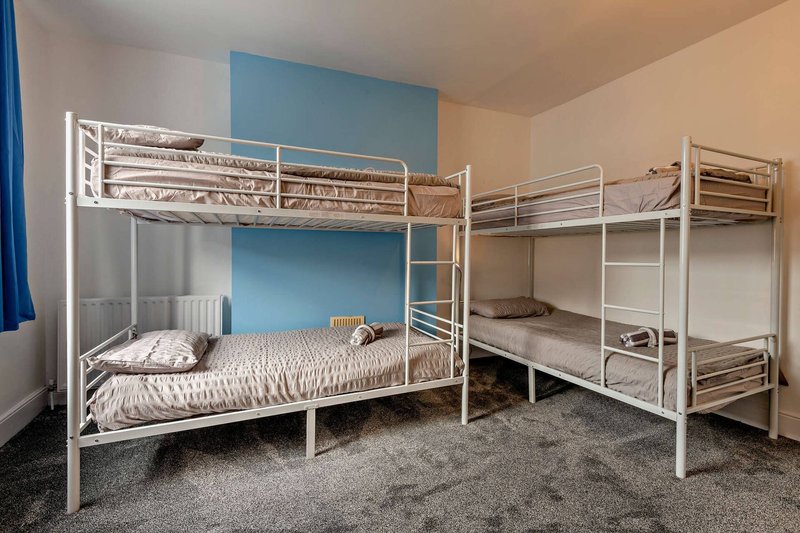 Dormitory bedroom with four white metal bunk beds, blue accent wall, and carpeted floor
