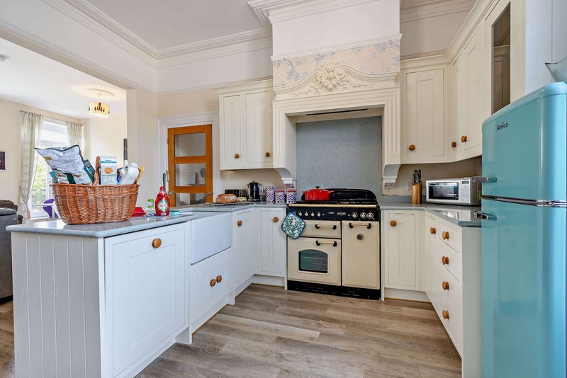 Retro-style kitchen with white cabinetry, turquoise fridge, cream Aga cooker and wicker basket