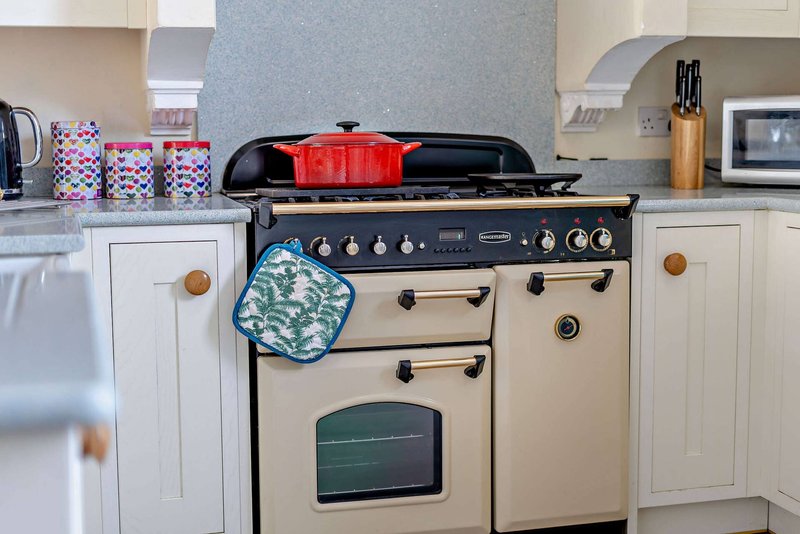 Kitchen with cream Aga-style cooker, red pot, patterned storage containers and wooden utensil holder