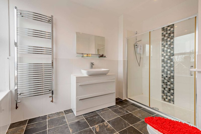 Modern bathroom with white vanity, vessel sink, heated towel rail, and shower enclosure