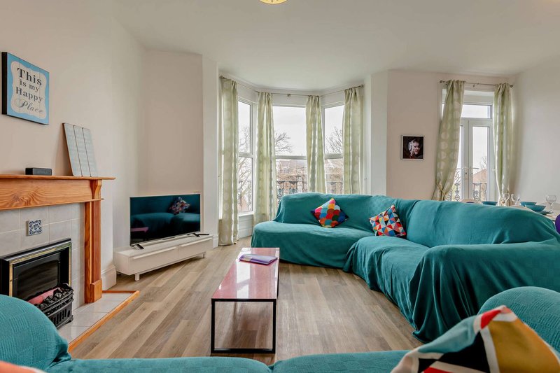 Bright living room with turquoise sectional sofa, wooden fireplace, bay windows and wooden flooring