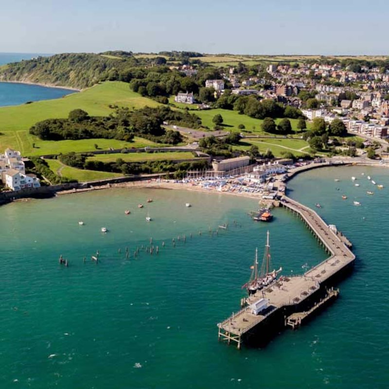 Aerial view of coastal town with beach, pier, green hills and turquoise water