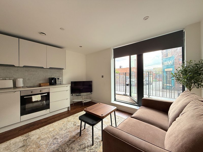 Modern open-plan studio with white kitchen, living area, sofa, and balcony with city views