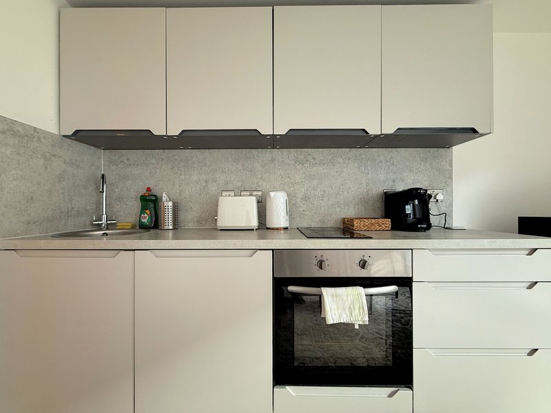 Modern white kitchen with grey splashback, built-in oven and countertop appliances