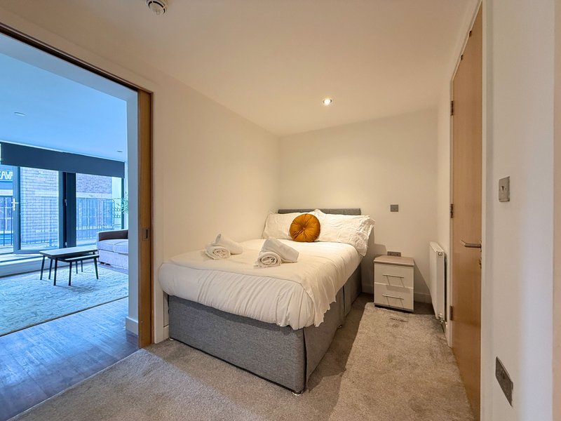 Modern bedroom with double bed, bedside table, and open door to living area with city views