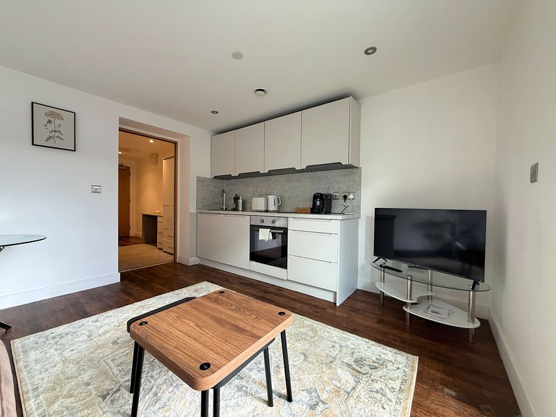 Open-plan living room and kitchen with white cabinetry, wooden dining table and TV on stand