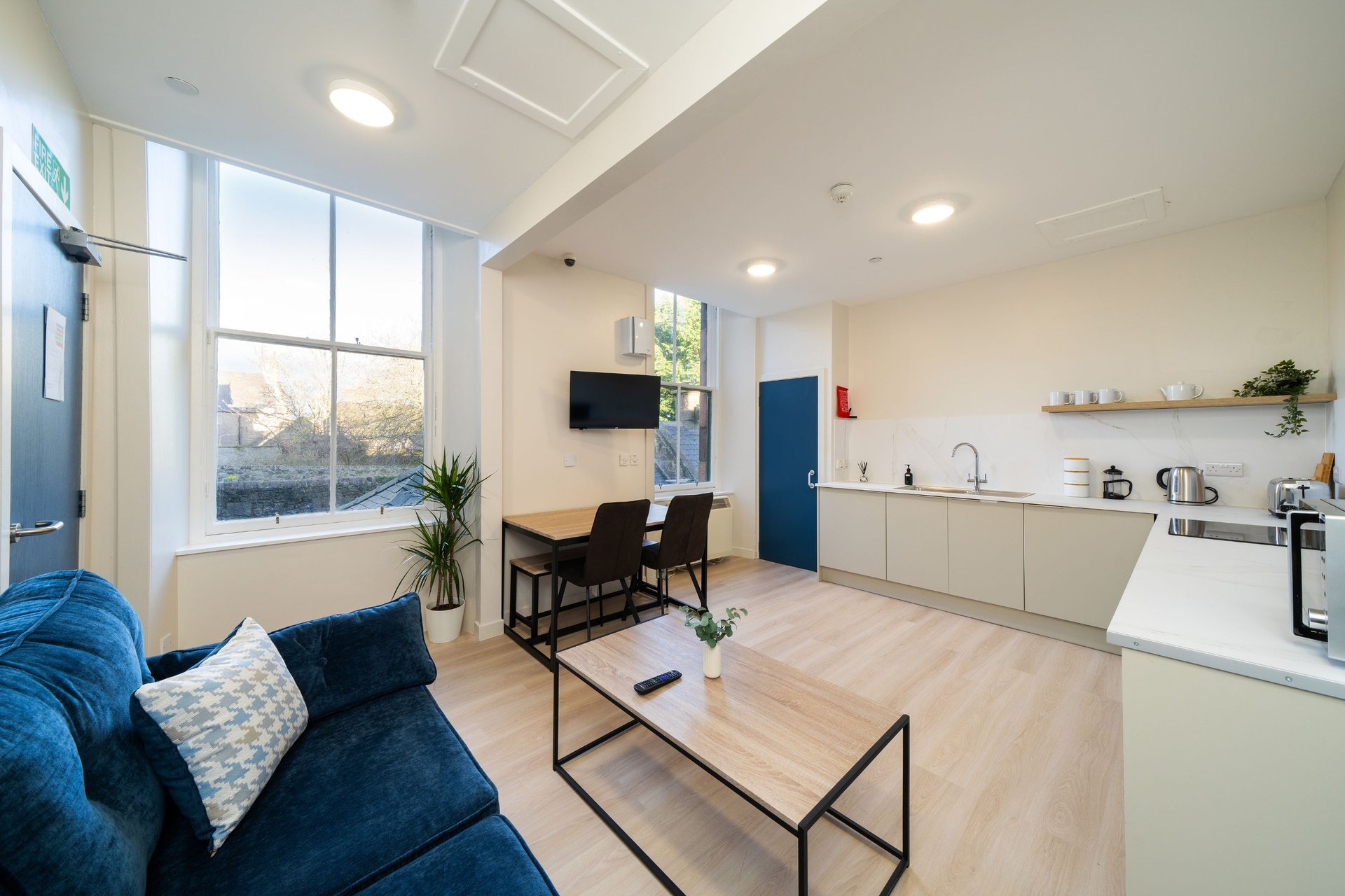 Modern open-plan living space with blue sofa, kitchen area, dining table and wall-mounted TV