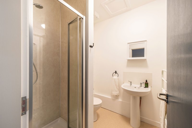 Clean bathroom with shower cubicle, pedestal sink, toilet and small window