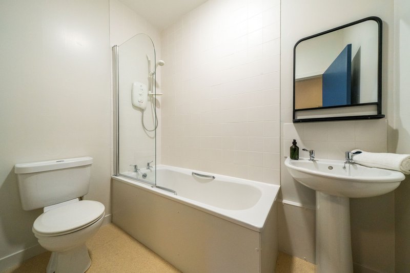 Modern bathroom with toilet, pedestal sink, bath with shower screen and mirror