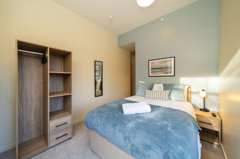 Modern bedroom with double bed, blue bedcover, wooden wardrobe and bedside tables