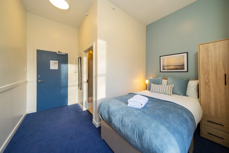Bedroom with blue door, double bed, wooden wardrobe and landscape artwork on wall