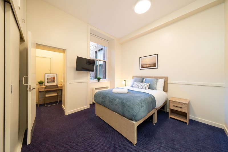 Bedroom with double bed, bedside table, desk area, and window with blue curtains