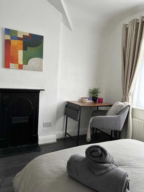 Bright bedroom with fireplace, desk, chair, bed with rolled towels, and colorful wall art