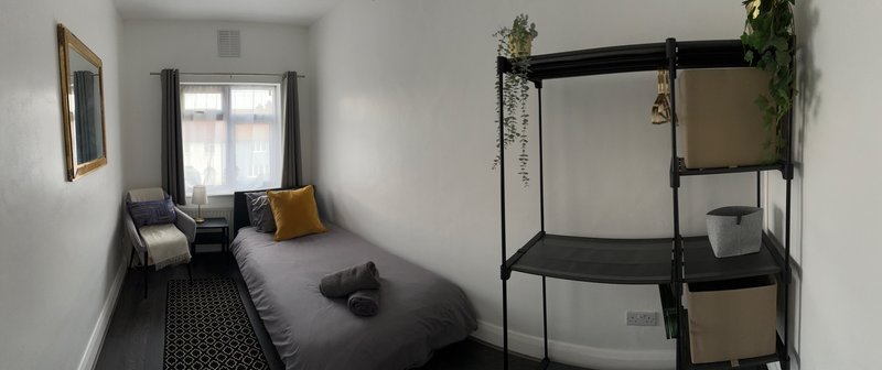 Compact bedroom with single bed, window seat area, and black metal shelving unit with plants