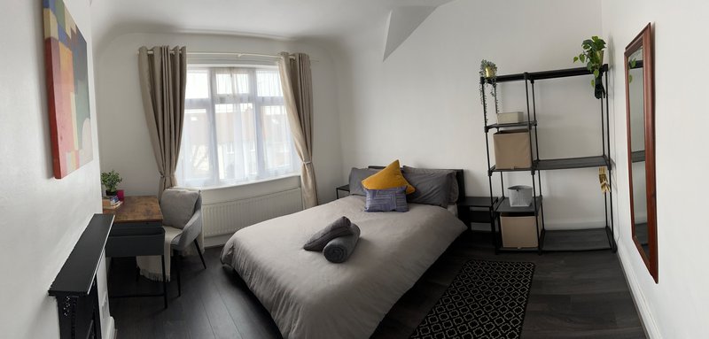 Bright bedroom with double bed, desk, shelving unit, and large window with curtains