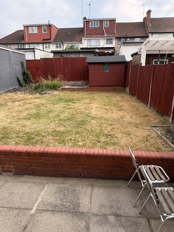 Rear garden with paved patio, brick border, lawn, and red wooden fence with gate