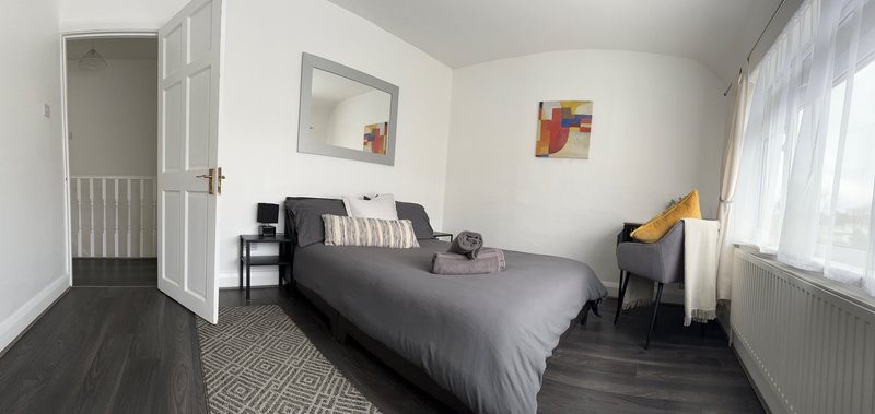 Bright bedroom with double bed, dark wooden floor, white walls and window with curtains
