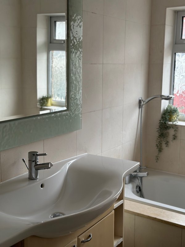 Modern bathroom with white curved sink, mirror, window, and bathtub with shower
