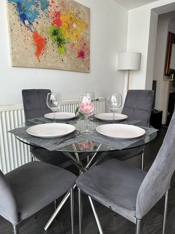 Modern dining room with round glass table, grey upholstered chairs, place settings and colourful abstract wall art