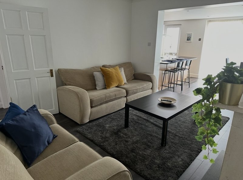 Modern living room with two beige sofas, black coffee table, potted plant, and open-plan kitchen view