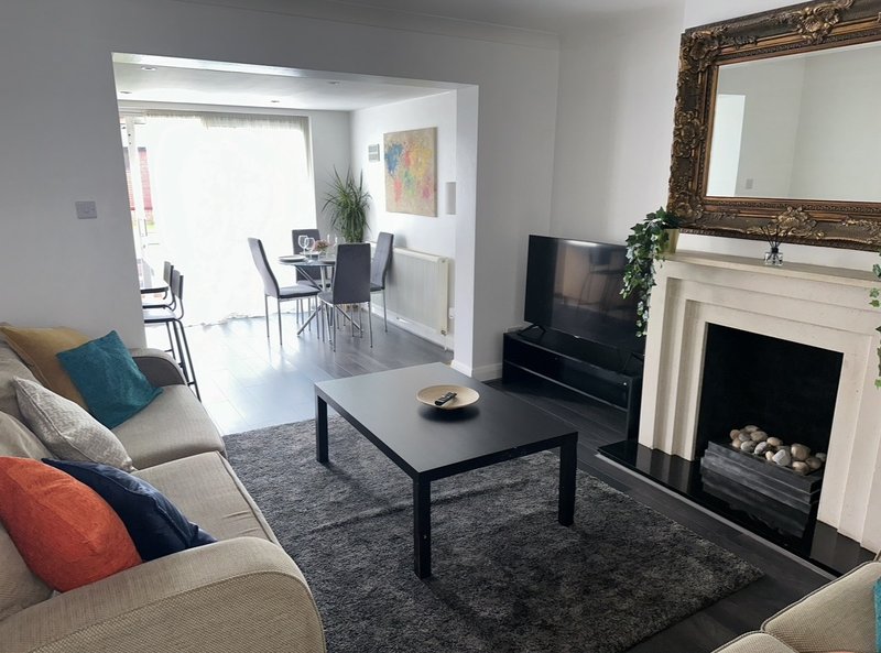 Modern living room with cream sofa, fireplace, TV, and dining area visible through doorway