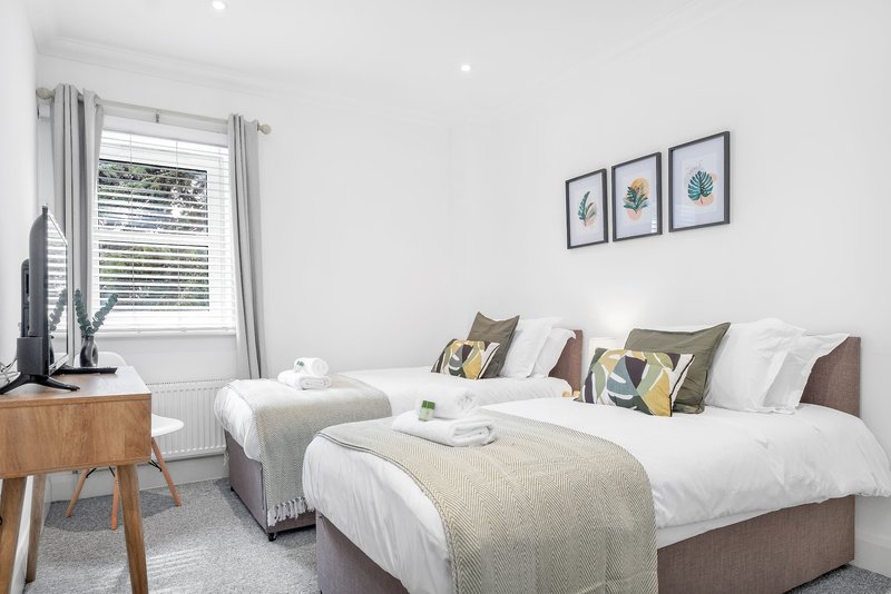 Twin bedroom with two single beds, wooden bedside table, window with curtains, wall art