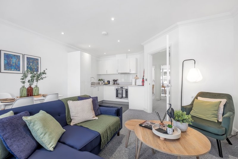 Open-plan living room with blue sofa, green armchair, wooden coffee table and white kitchen