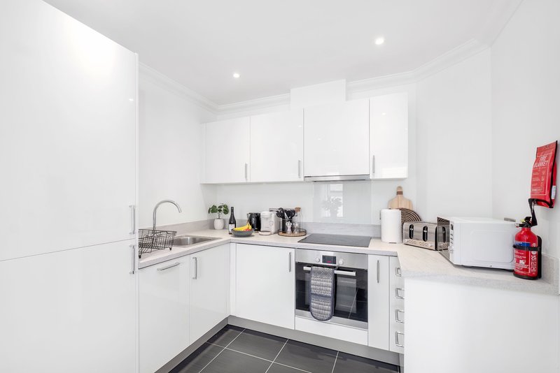 Modern white kitchen with integrated appliances, sink, countertops and dark tile flooring