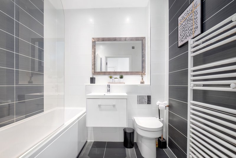 Modern bathroom with white sink, toilet, bathtub, heated towel rail and framed mirror