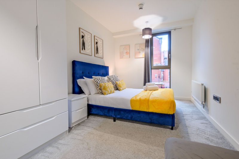 Modern bedroom with blue velvet bed, yellow bedding, white wardrobe and city view window